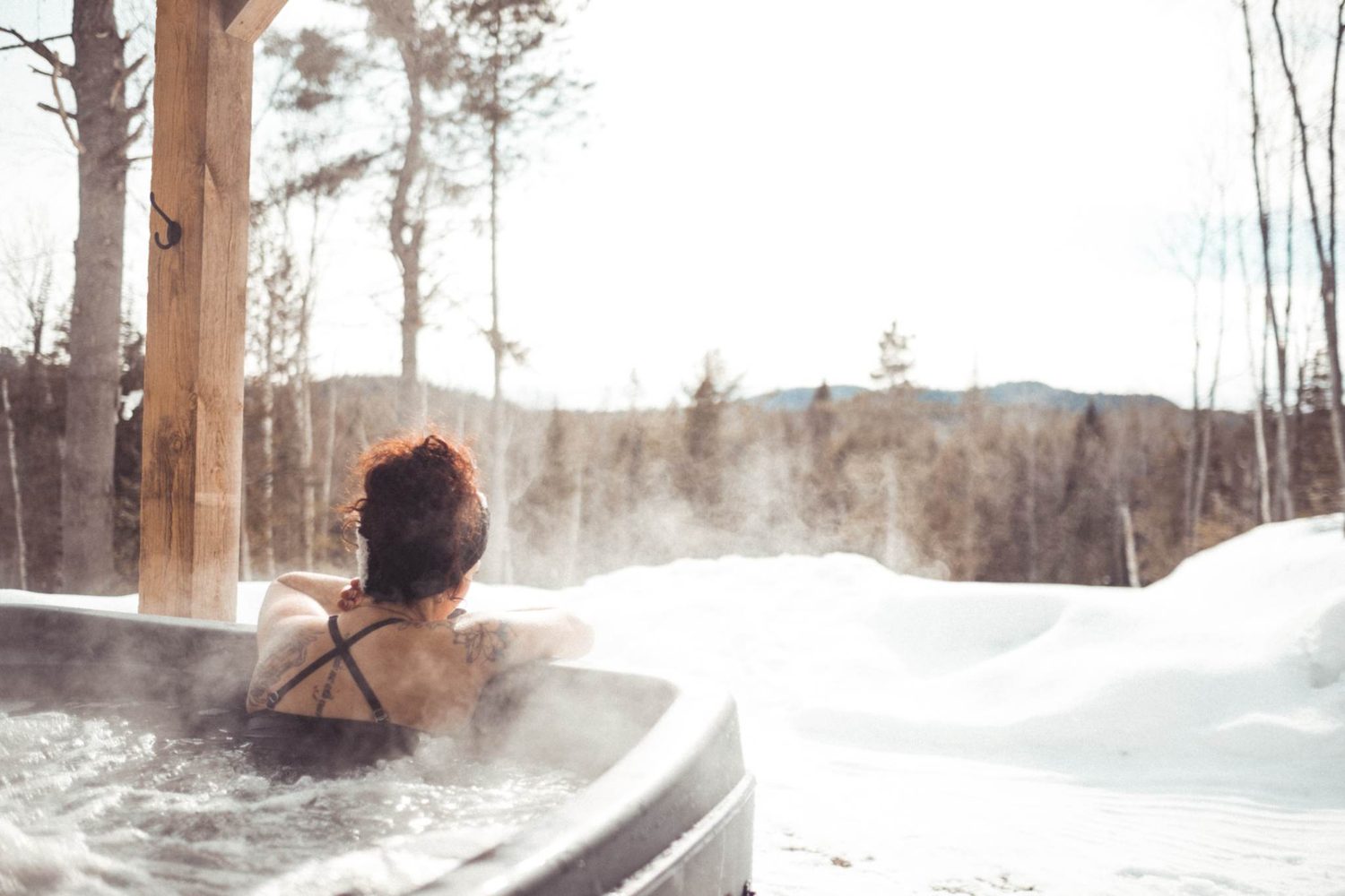 Un spa extérieur fumant devant la forêt enneigée, au petit matin.