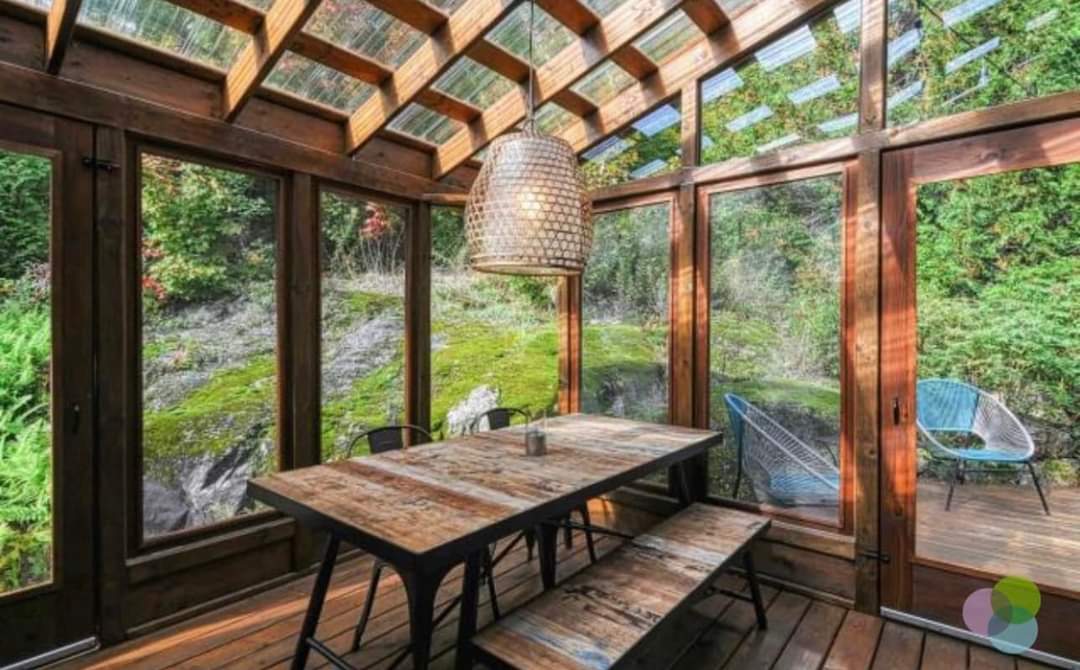 Solarium vitré sur la forêt, longue table de bois et bancs.